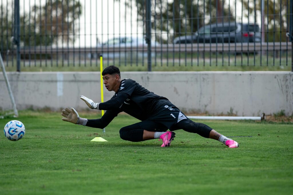 Goalkeeper practicing on a green grass field, focused on saving a soccer ball.